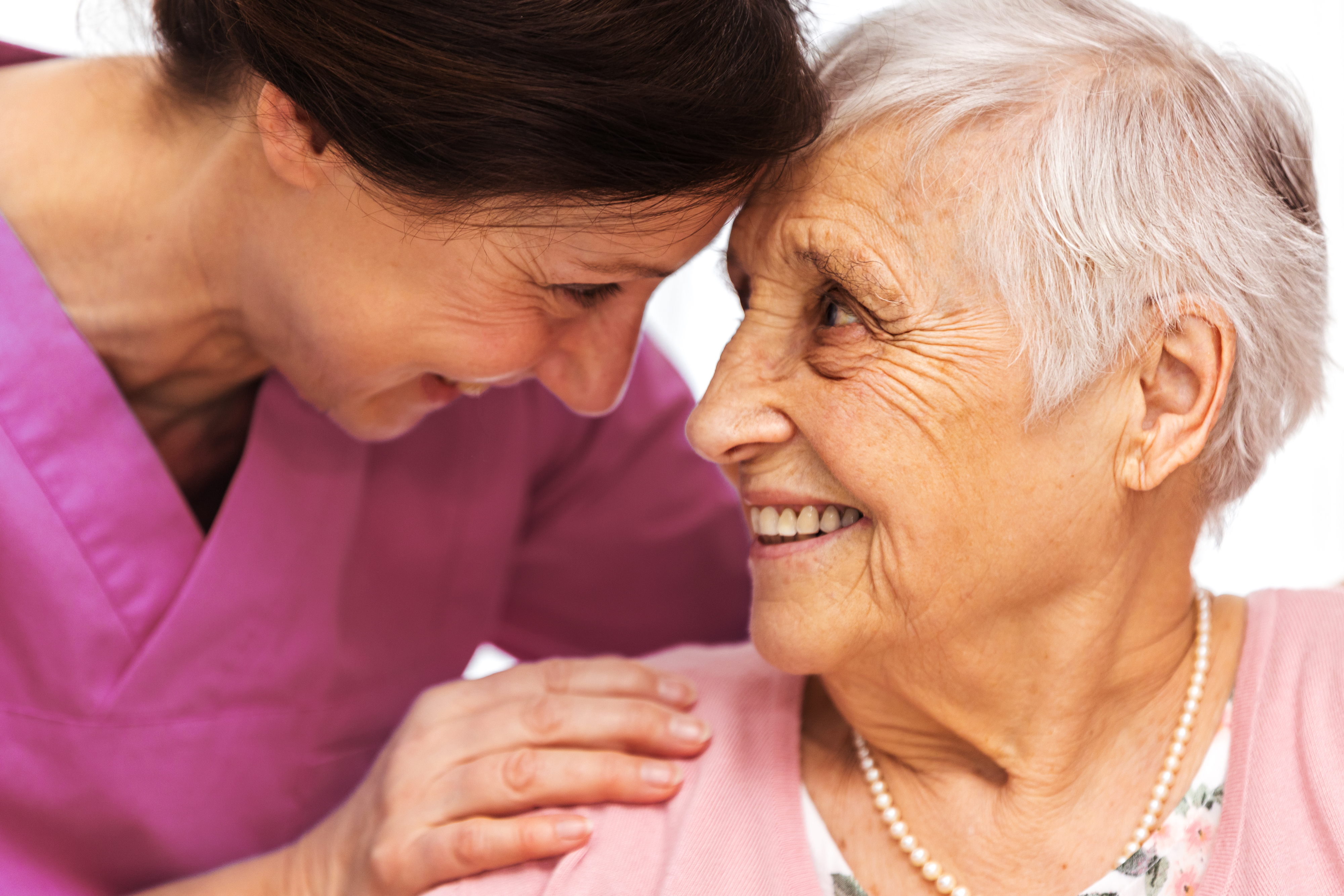 Eine Pflegerin hilft einer älteren Frau mit der Hand auf der Schulter.