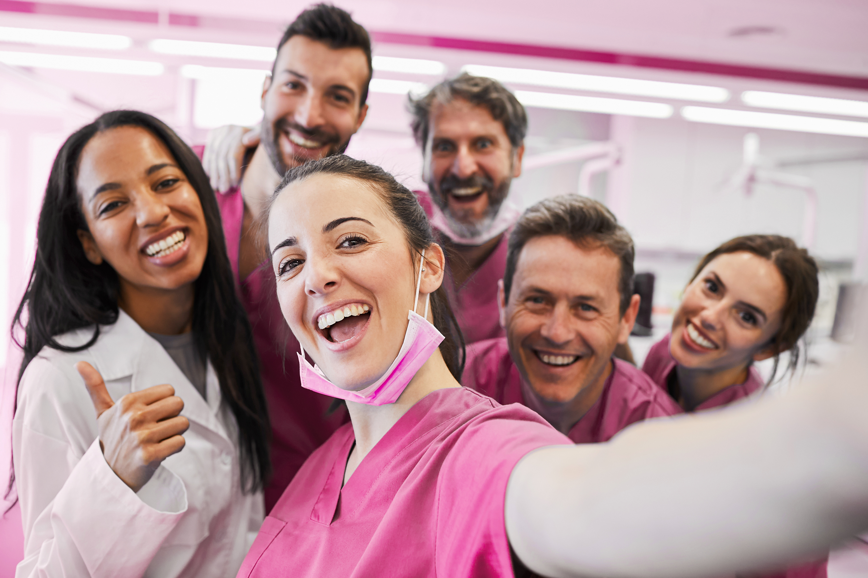 Eine Gruppe von Pfleger:innen in rosa Dienstkleidung, die für ein Selfie posieren.